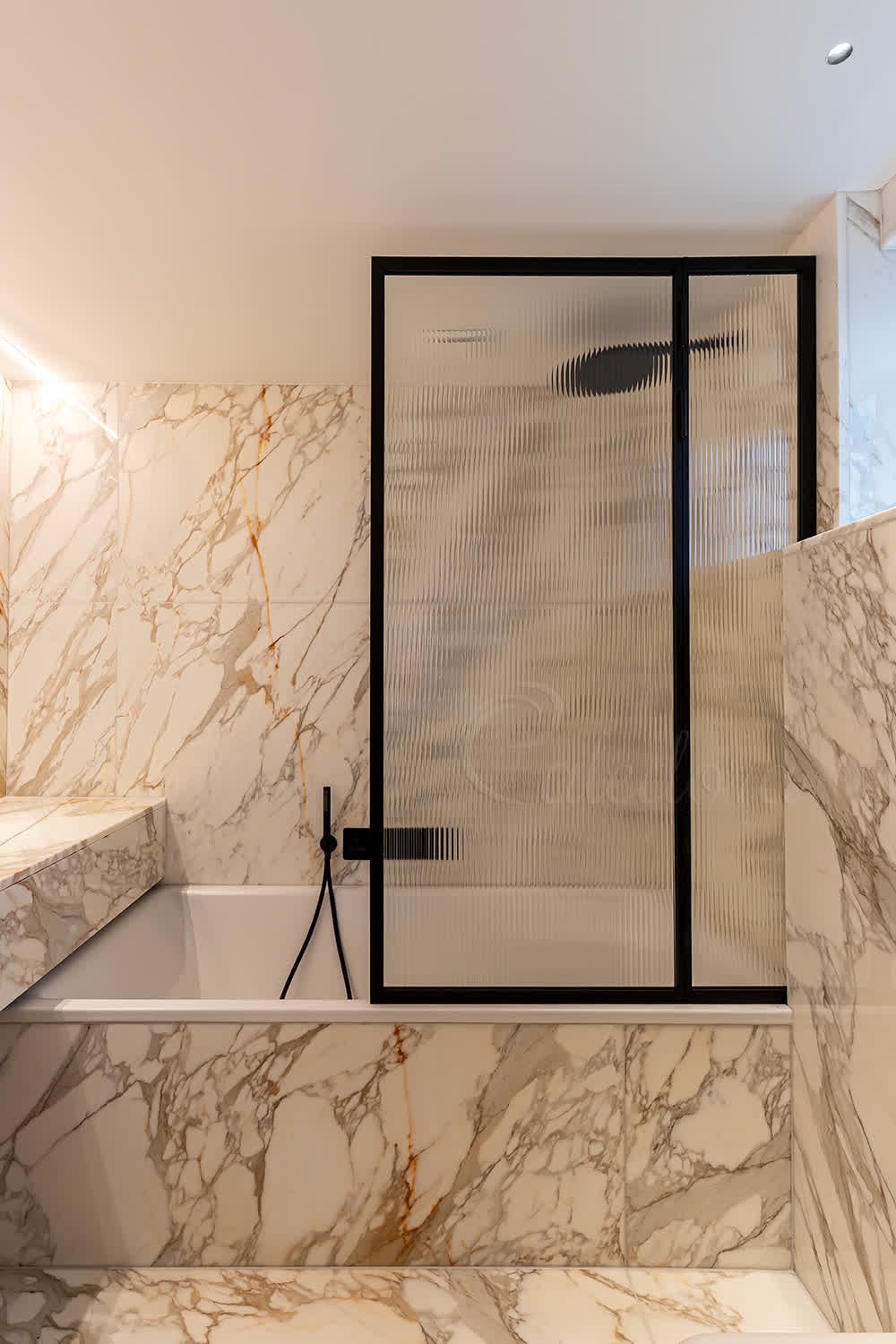 Black framed folding bath screen closed position with reeded glass against luxury marble walls