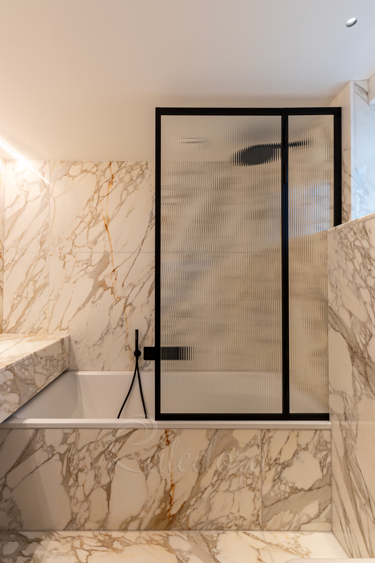 Elegant black framed folding bath screen with reeded glass in a luxury marble bathroom