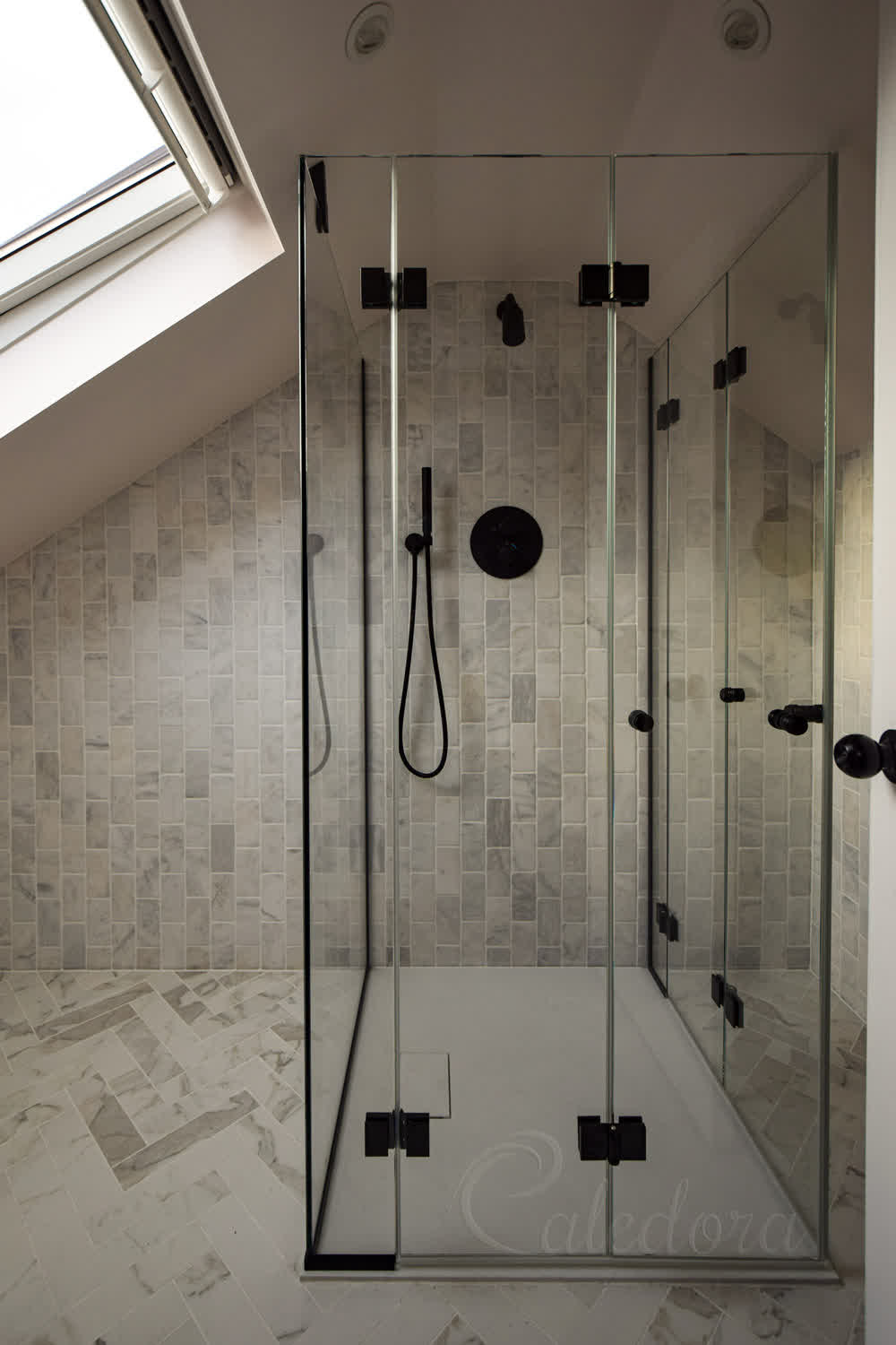Black bifold shower door in corner enclosure with ultra clear glass in a small loft bathroom