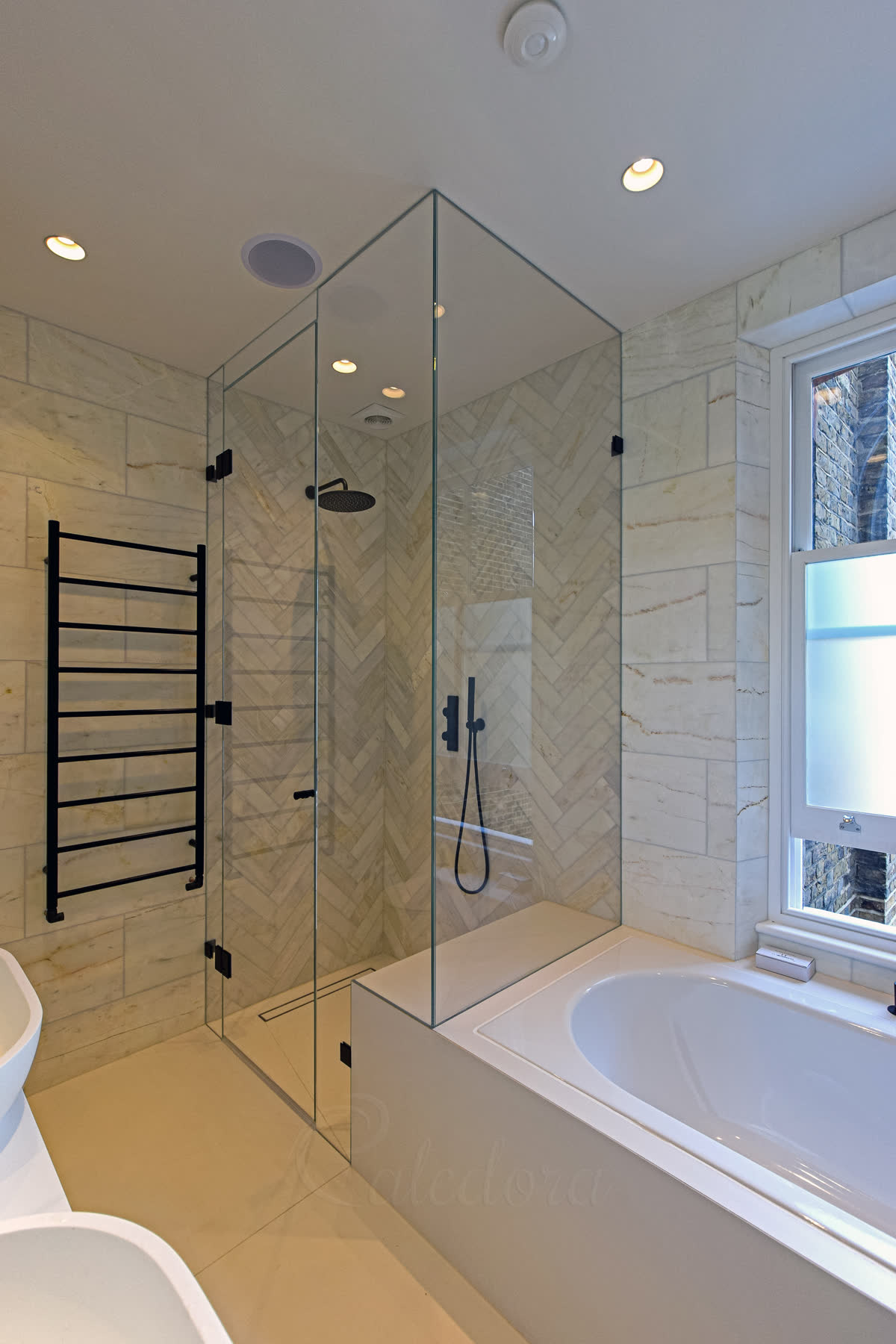 Black frameless corner shower enclosure over bath with door closed showing marble tiles