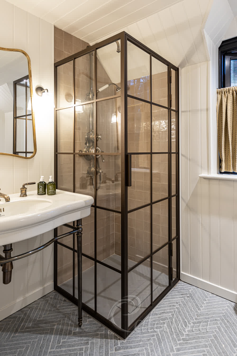 Corner bronze shower enclosure with grid design installed between tiled walls and wooden panelling