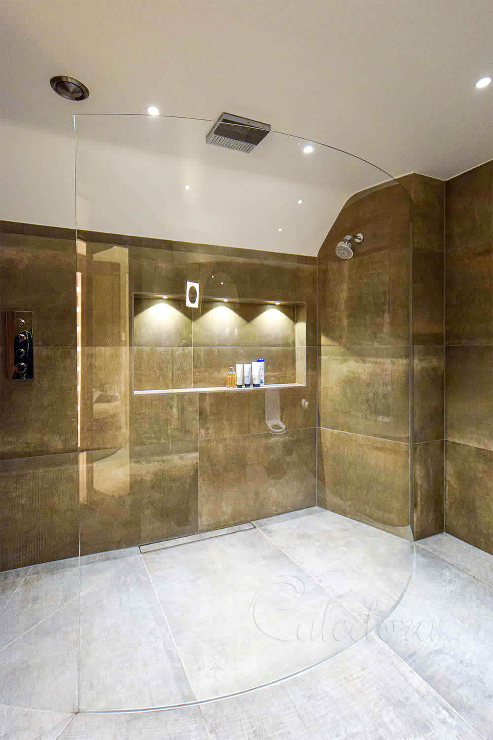 Frameless curved shower screen in luxury master bathroom with golden stone tiles