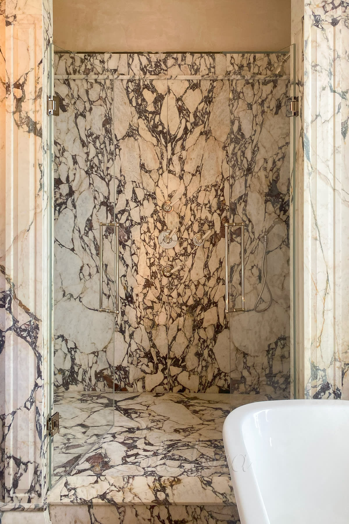 Double shower doors partially open inwards showing marble walls and ultra clear glass panels