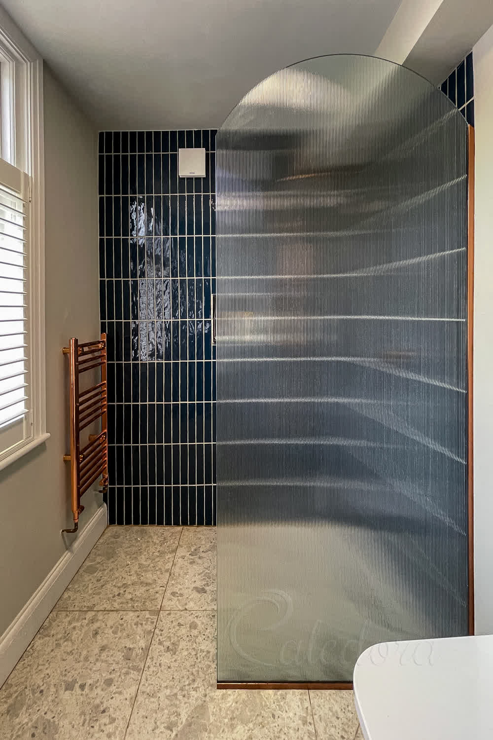 Fluted glass arched shower screen with copper U-channels in London bathroom