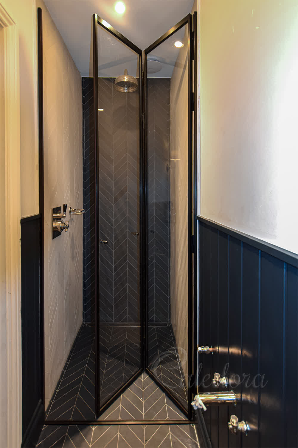 Black framed folding shower door in London with herringbone tile pattern