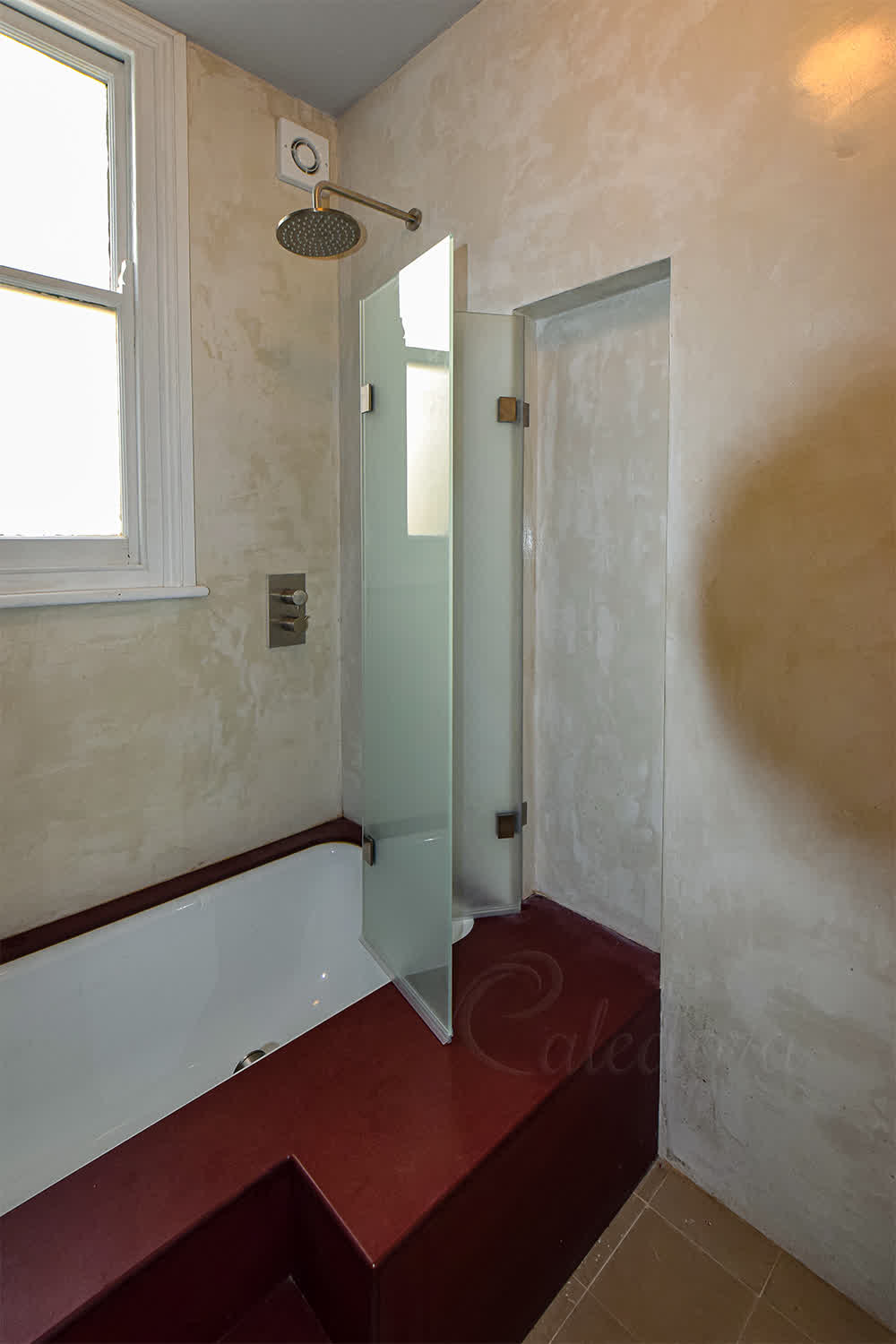 Folding shower screen with frosted glass on a red bath surround in London bathroom