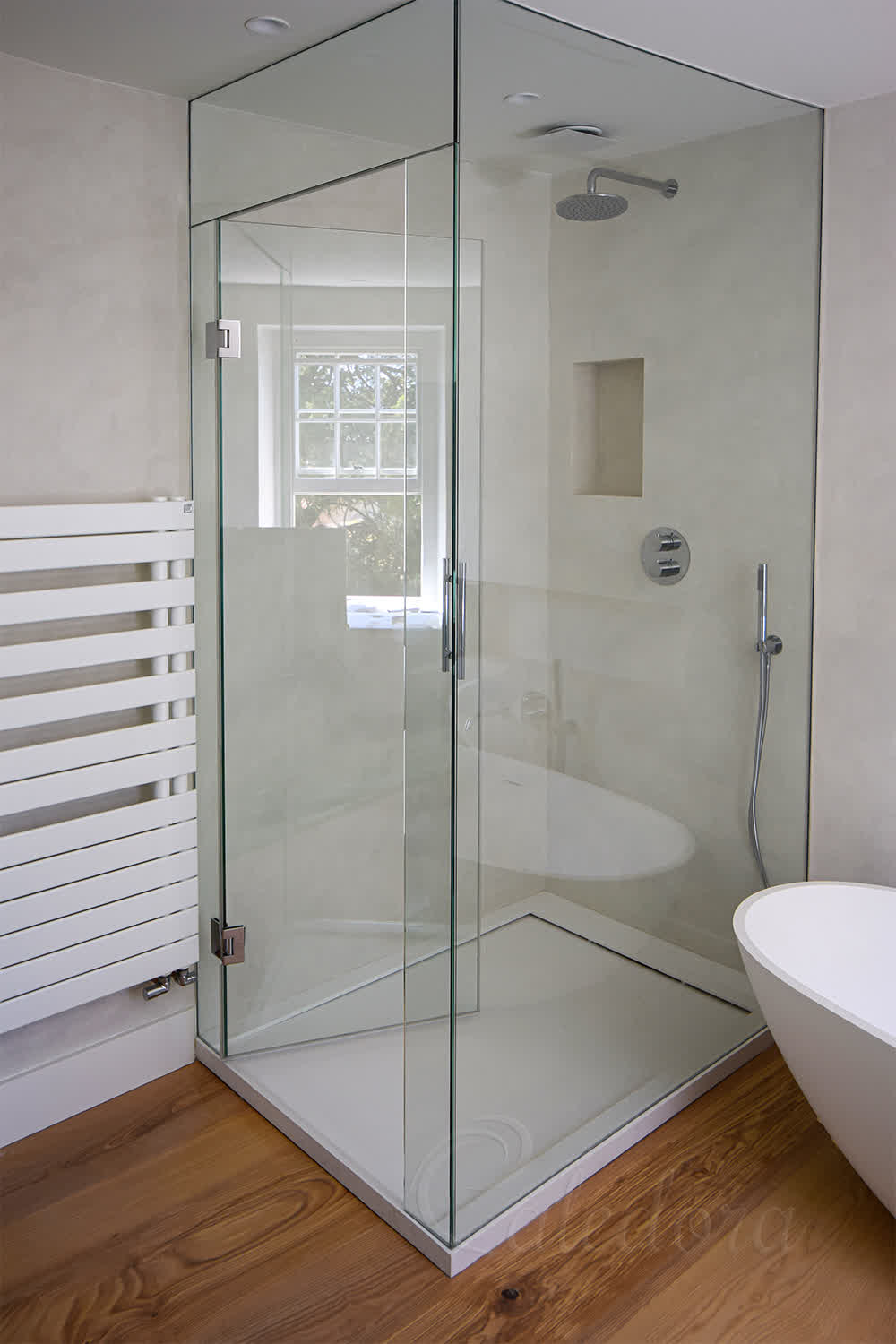 Floor to ceiling shower enclosure in corner bathroom with towel radiator and freestanding bath
