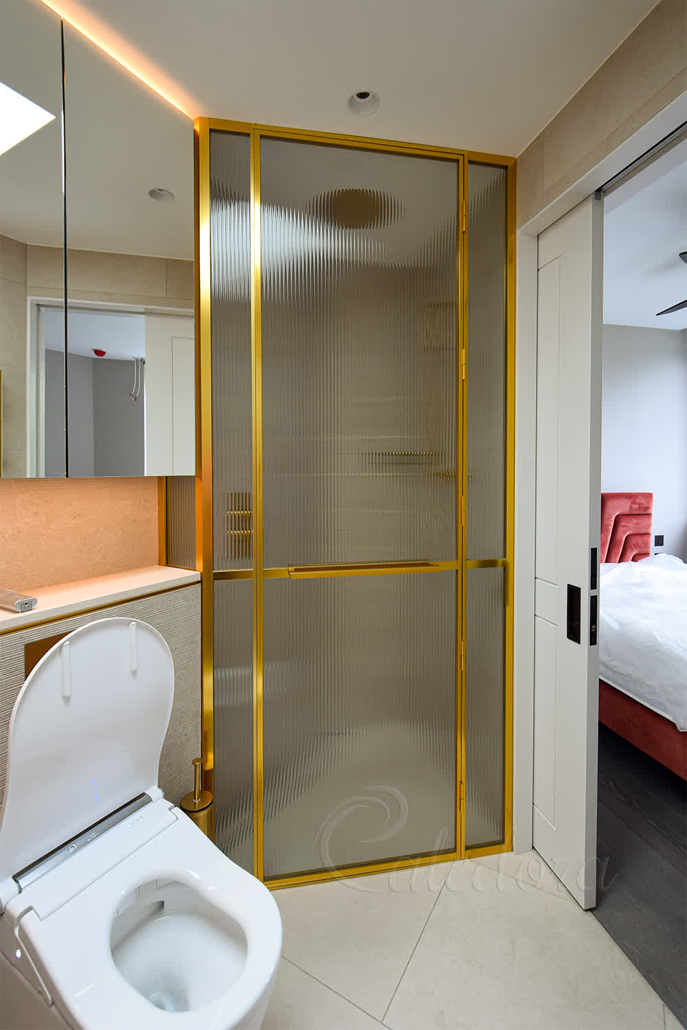 Gold shower enclosure with fluted glass and bespoke towel rail aligned with half-wall stone top