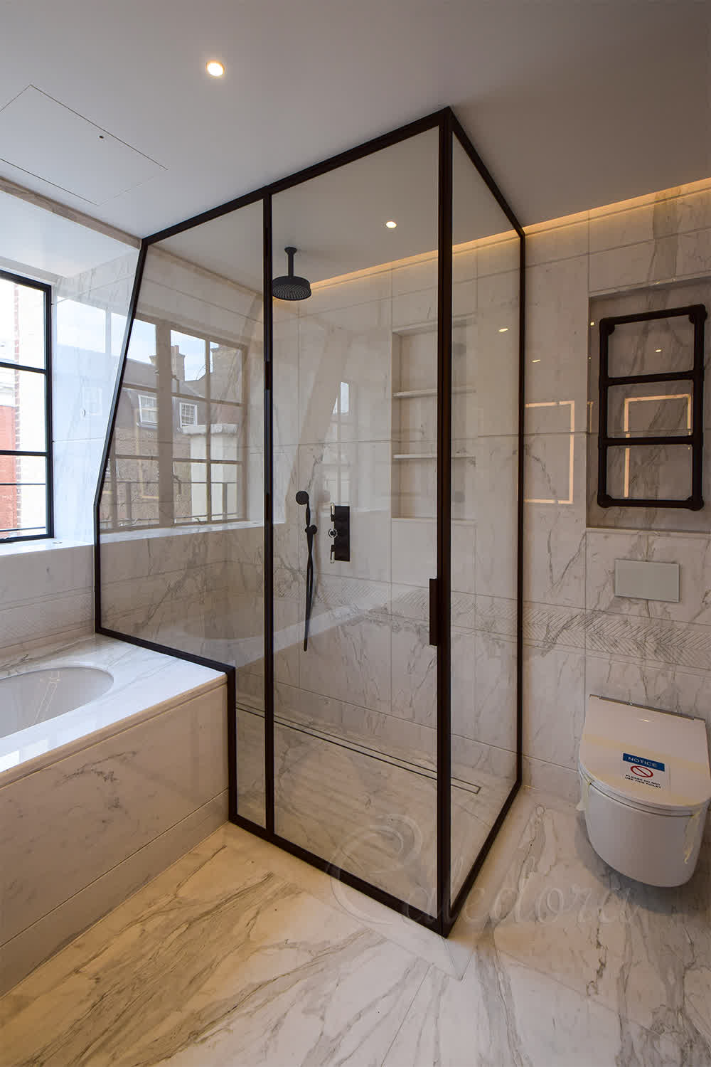 Bronze framed shower enclosure fitted over bath with custom glass cut following the bath's contour in a marble bathroom
