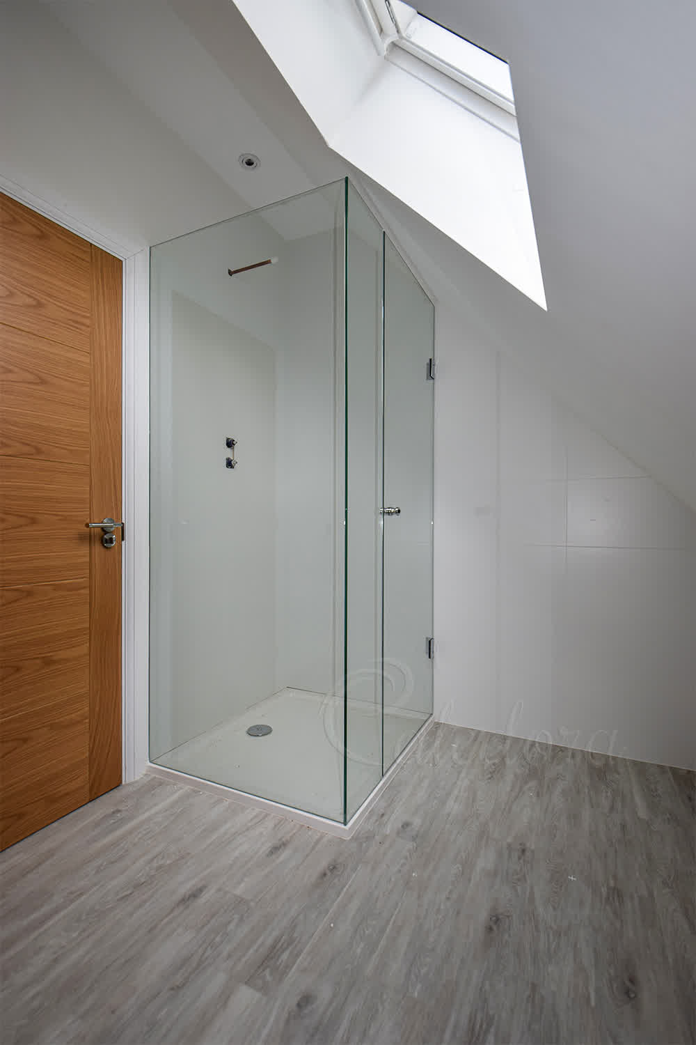 Frameless shower enclosure with hinged door in corner under sloped ceiling