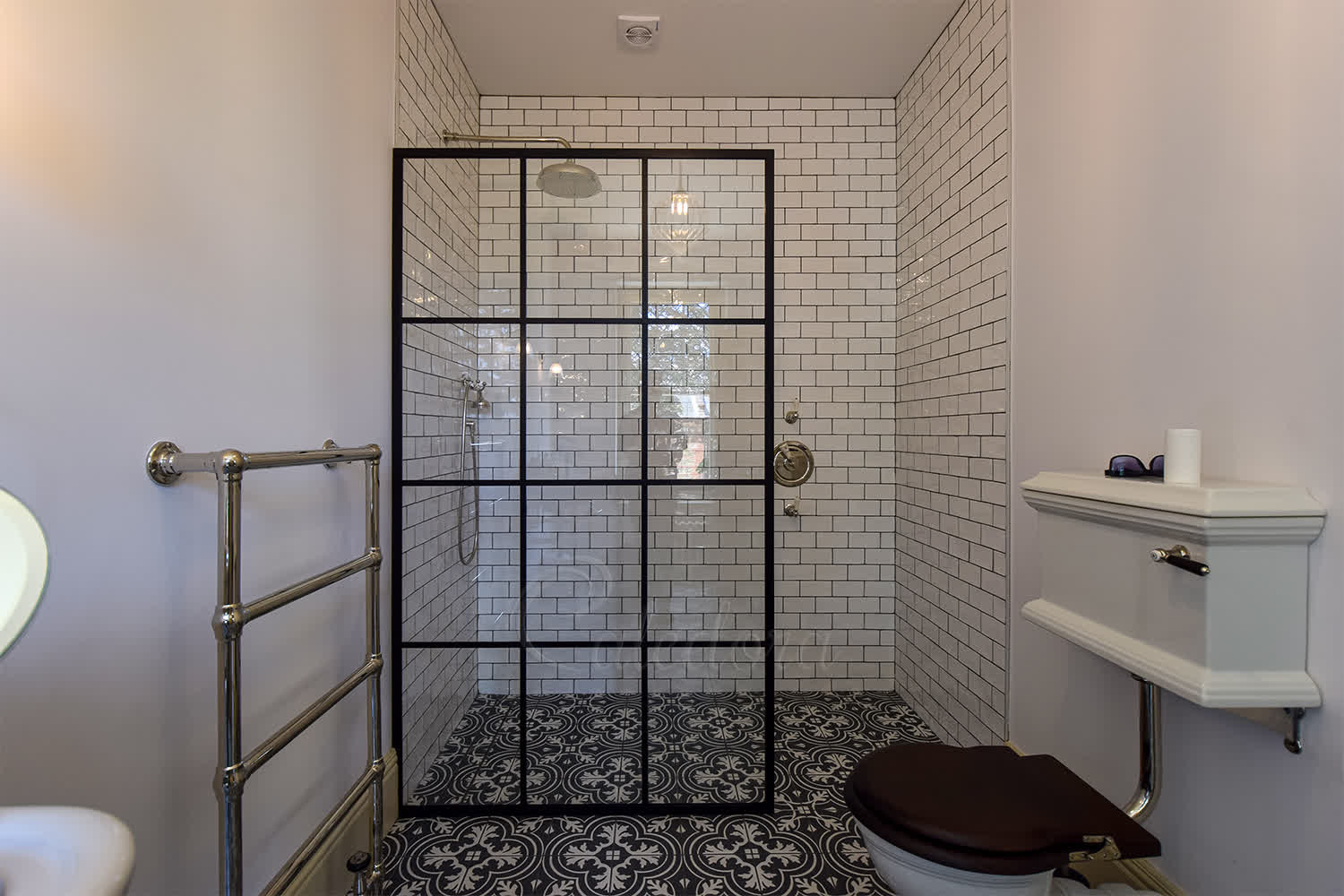 Elegant black grid shower screen with beige subway tile walls and patterned floor in London bathroom