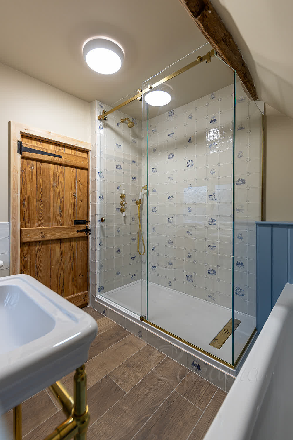Frameless sliding shower enclosure with brass hardware in traditional bathroom with blue half-wall