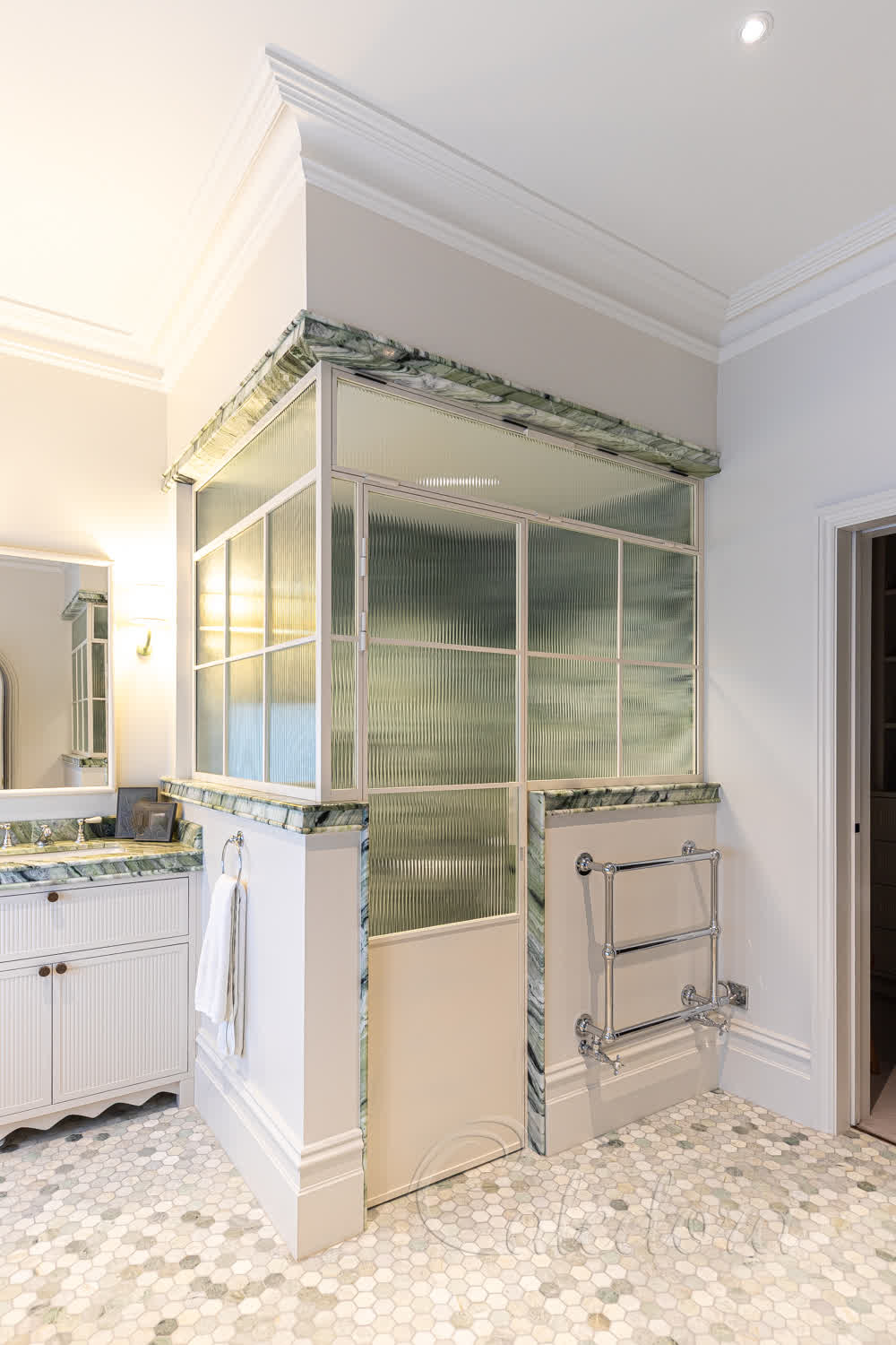 White grid shower enclosure with fluted glass and bottom panelling featuring a closed door in a luxury bathroom with marble floors